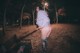 A woman standing on a bench in a park at night.