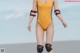 A woman in a yellow swimsuit and knee pads walking on the beach.