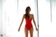 A woman in a red bathing suit standing in front of a window.